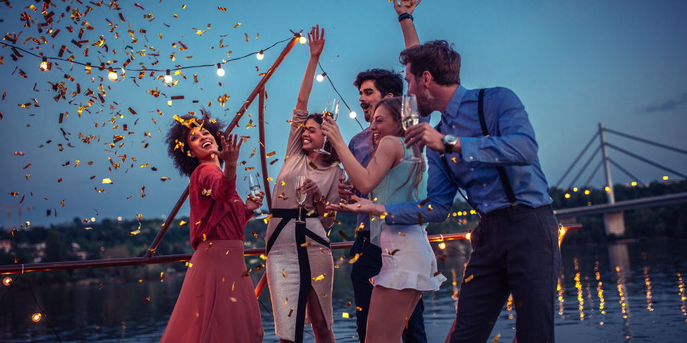 Friends celebrating under confetti on a boat deck at dusk